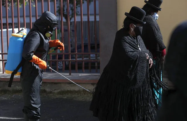 A funeral home worker wearing full protective gear as a precaution against the spread of the new coronavirus sprays disinfectant over the relatives the late Guillermo Carpio, outside the General Hospital in La Paz, Bolivia, Wednesday, July 22, 2020. Herminia Carpio said her 58-year-old brother died the previous afternoon, and according to the hospital he died from COVID-19 complications. (Photo by Juan Karita/AP Photo)