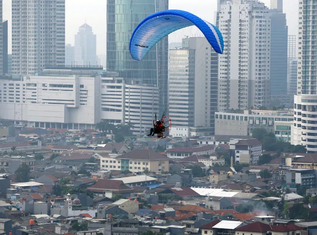 A pilot guides his powered paraglider while flying above central Jakarta, Indonesia September 25, 2016. (Photo by Darren Whiteside/Reuters)