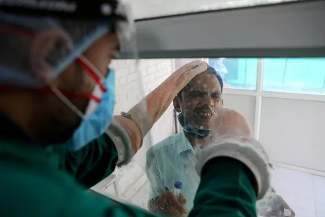 A healthcare worker collects a swab sample from a man amidst the spread of the coronavirus disease (COVID-19), at a testing centre, in New Delhi, India October 9, 2020. (Photo by Anushree Fadnavis/Reuters)