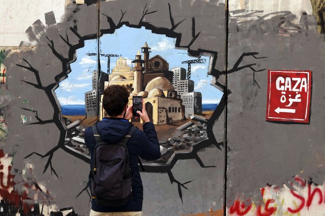A man takes a picture of graffiti representing the reconstruction of Gaza, on a section of Israel's separation barrier, in Bethlehem in the occupied West Bank on February 12, 2025. Mediators Qatar and Egypt were pushing to resolve a crisis in the Gaza ceasefire, a Palestinian source told AFP, after Israel and the United States told Hamas to release hostages this weekend or face a return to war. (Photo by Hazem Bader/AFP Photo)