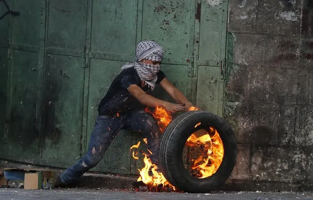 A young Palestinian protester pushes a burning tyre during clashes with Israeli troops in the West Bank city of Hebron October 31, 2015. Israeli security forces shot and killed a Palestinian who ran at them with a knife in the occupied West Bank on Saturday, police said, as a month-long wave of violence showed no signs of abating. (Photo by Ammar Awad/Reuters)