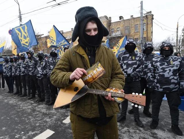 An activist holding a balalayka instrument, part of a group of Ukrainian nationalists protesting a voting ban imposed to Russian citizens living in Ukraine, gives out “ballots” to Russian citizens living in Ukraine during a picket by Ukrainian nationalists outside the Russian embassy in Kiev on March 18, 2018. Kiev has said Russians living in Ukraine would not be able to vote in today's election as access to Moscow's diplomatic missions would be blocked. (Photo by Sergei Supinsky/AFP Photo)
