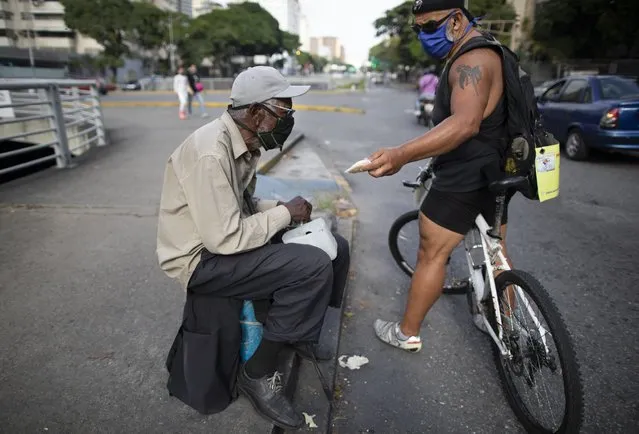 Andres Burgos, a 55-year-old publicist, gives a package of arepas or corn flour patties to a man begging for money at a traffic light in Caracas, Venezuela, Tuesday, October 20, 2020. Burgos hands out his homemade arepas from the seat of his bicycle to needy children, adults and the elderly. He calls it BiciArepazo, which translates roughly as Bike Arepas. (Photo by Ariana Cubillos/AP Photo)