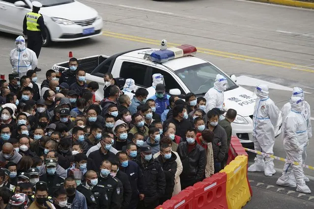 Security workers in protective suits stand by as workers wearing face masks to help curb the spread of the coronavirus gather for COVID-19 testing at the Shanghai Pudong International Airport in Shanghai, Monday, November 23, 2020. Chinese authorities are testing millions of people, imposing lockdowns and shutting down schools after multiple locally transmitted coronavirus cases were discovered in three cities across the country last week. (Photo by AP Photo/Stringer)