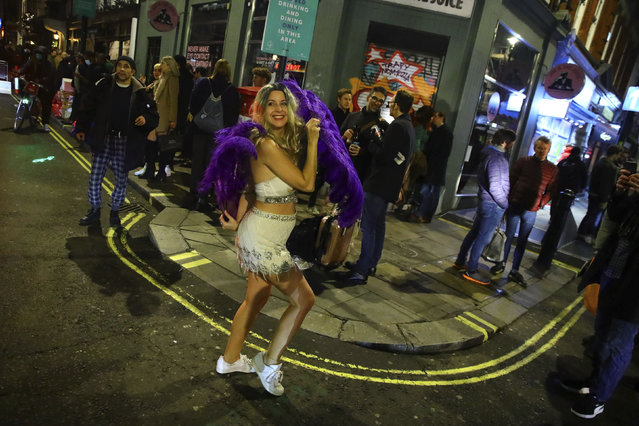 A woman dances with purple feathers in the West End of London after pubs close, before London moves into the highest tier of coronavirus restrictions from Wednesday as a result of soaring case rates, Tuesday December 15, 2020. (Photo by Aaron Chown/PA Wire via AP Photo)