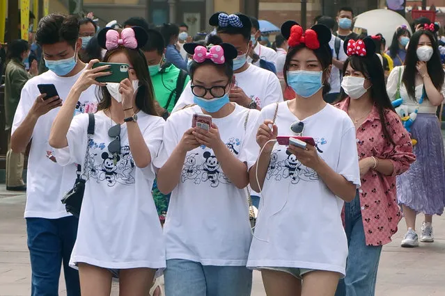 Visitors, wearing face masks, enter the Disneyland theme park in Shanghai as it reopened, Monday, May 11, 2020. Visits will be limited initially and must be booked in advance, and the company said it will increase cleaning and require social distancing in lines for the various attractions. (Photo by Sam McNeil/AP Photo)