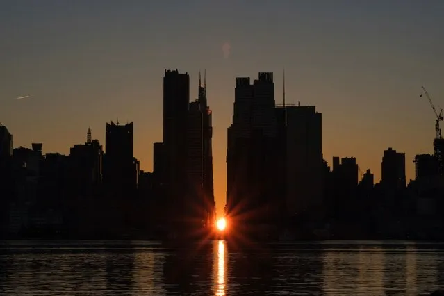 The sun rises through the middle of buildings long 42nd street in New York's Manhattan borough during a phenomenon known as Manhattanhenge on Sunday, November 29, 2020, as viewed from Weehawken, N.J. Manhattanhenge is when the rising sun intersects with the Manhattan street grid. (Photo by Yuki Iwamura/AP Photo)