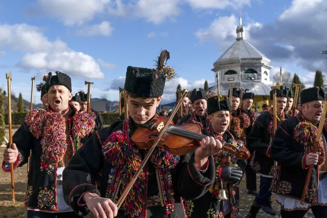 An ethnic Hutsul man, an ethnic group spanning parts of western Ukraine, plays a violin as others, all wearing traditional colorful clothes, sing a kolyada song during the Orthodox Christmas celebration near the Holy Trinity church in Iltsi village, Ivano-Frankivsk region of Western Ukraine, Thursday, January 7, 2021. Orthodox Christians celebrate Christmas on Jan. 7, in accordance with the Julian calendar. (Photo by Evgeniy Maloletka/AP Photo)