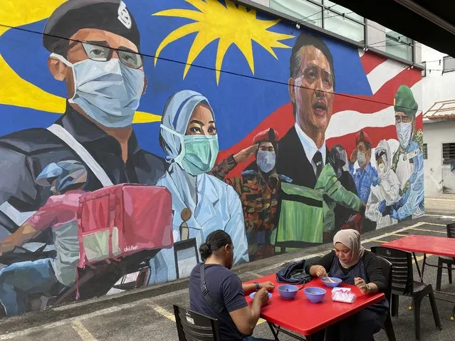 A Malay couple have lunch next to a graffiti tribute to Malaysian workers on the frontlines against the COVID-19 coronavirus at Damansara in Selangor, outside Kuala Lumpur, Malaysia, Saturday, November 7, 2020. Malaysia extended restricted movements in its biggest city Kuala Lumpur, neighboring Selangor state and the administrative capital of Putrajaya from Wednesday in an attempt to curb a sharp rise in coronavirus cases. (Photo by Vincent Thian/AP Photo)