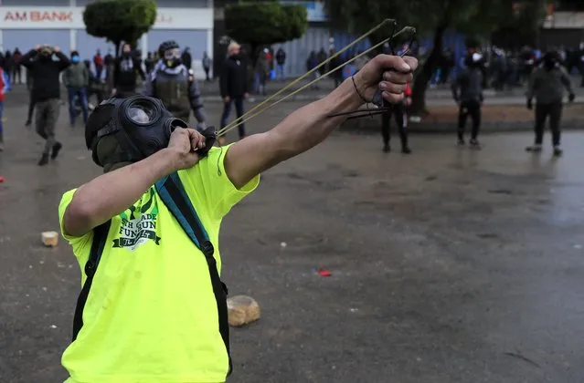 A protester fires a slingshot towards riot policemen during a protest against deteriorating living conditions and strict coronavirus lockdown measures, in Tripoli, north Lebanon, Thursday, January 28, 2021. Violent confrontations for three straight days between protesters and security forces in northern Lebanon left a 30-year-old man dead and more than 220 people injured, the state news agency said Thursday. (Photo by Hussein Malla/AP Photo)