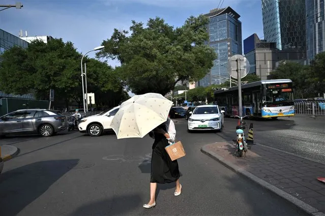 A woman carries an umbrella during a heatwave in Beijing on June 23, 2023. China issued its highest-level heat alert for northern parts of the country on June 23 as the capital baked in temperatures hovering around 40 degrees Celsius (104 Fahrenheit). (Photo by Greg Baker/AFP Photo)