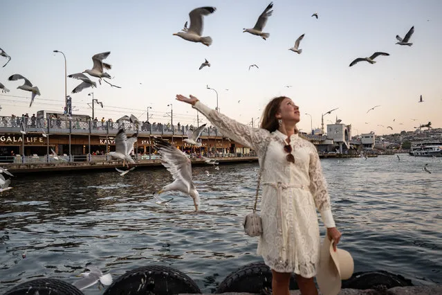 A woman poses for a photo with seagulls as historical peninsula and surroundings are seen in the back during sunset in Istanbul, Turkiye on June 22, 2023. (Photo by Cem Tekkesinoglu/Anadolu Agency via Getty Images)