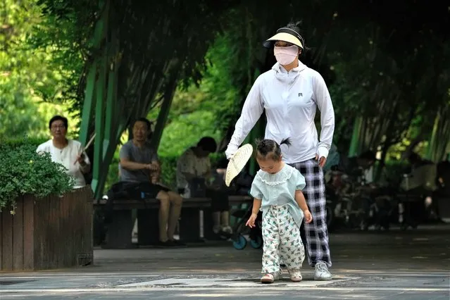 A woman uses a fan to cool a child as residents rest in a shade at a public park on a sweltering day in Beijing, Tuesday, July 18, 2023. (Photo by Andy Wong/AP Photo)