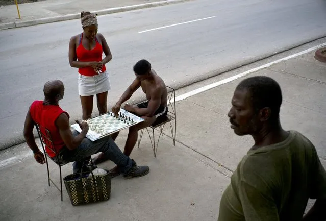 In this July 24, 2018 photo, a woman talks to men playing chess as another resident stands outside his home on the hot afternoon in Guantanamo, Cuba, near the U.S. Guantanamo Bay naval base. Chess games can be spotted on sidewalks and plazas across the island, where players tend to bet on no more than a cold beer. (Photo by Ramon Espinosa/AP Photo)