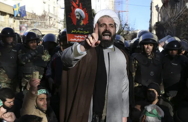 Surrounded by policemen, a Muslim cleric addresses a crowd during a demonstration to protest the execution of Saudi Shiite Sheikh Nimr al-Nimr, shown in the poster in background, in front of the Saudi embassy in Tehran, Iran, Sunday, January 3, 2016. Saudi Arabia announced the execution of al-Nimr on Saturday along with 46 others. Al-Nimr was a central figure in protests by Saudi Arabia's Shiite minority until his arrest in 2012, and his execution drew condemnation from Shiites across the region. (Photo by Vahid Salemi/AP Photo)