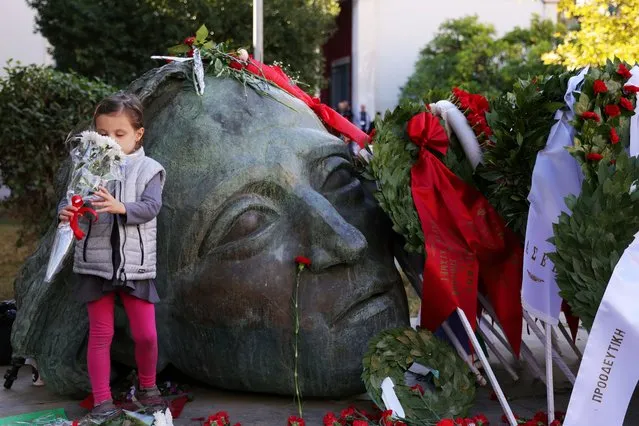 A child smells flowers in front of a monument inside the Athens Polytechnic, to mark the 50th anniversary of a 1973 student uprising against the military junta that ruled the country at the time, in Athens, Greece on November 16, 2023. (Photo by Louiza Vradi/Reuters)
