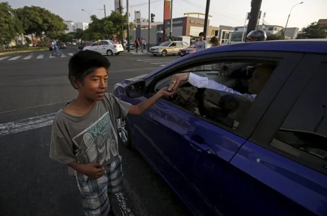 A boy receives a tip after doing somersaults at a traffic junction in Lima April 27, 2015. (Photo by Mariana Bazo/Reuters)