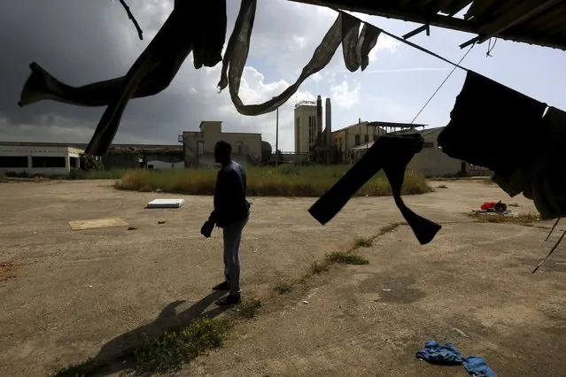 A Sudanese immigrant stands next to clothes that are hanging out to dry inside a deserted textile factory in the western Greek town of Patras April 28, 2015. (Photo by Yannis Behrakis/Reuters)