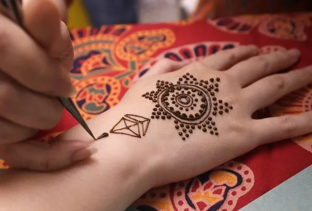 An artist applies henna on the hand or a woman during the Hindu festival of lights, Diwali, in Taipei, Taiwan, Thursday, November 4, 2021. Millions of people across Asia are celebrating the Hindu festival of Diwali, which symbolizes new beginnings and the triumph of good over evil and light over darkness. (Photo by Chiang Ying-ying/AP Photo)