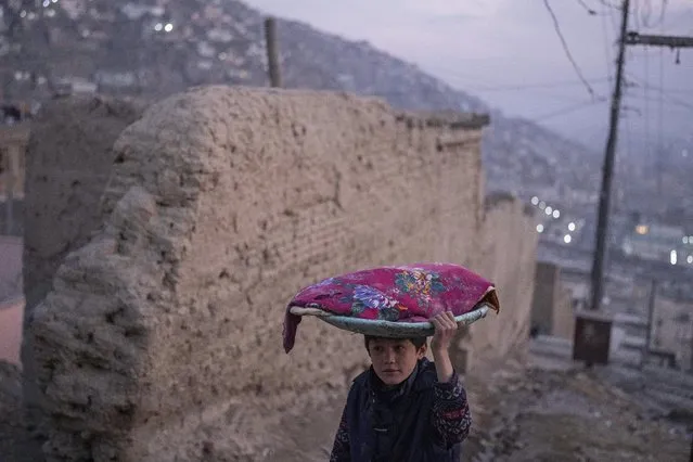 An Afghan boy carries a tray of bread on his head, in Kabul, Afghanistan, Sunday, December 5, 2021. (Photo by Petros Giannakouris/AP Photo)