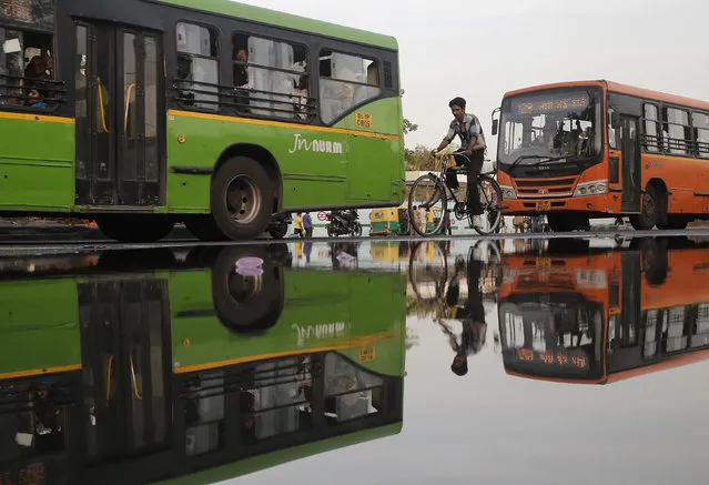A man cycles between buses along a puddle on a street in the old quarters of Delhi, India, April 1, 2016. (Photo by Anindito Mukherjee/Reuters)