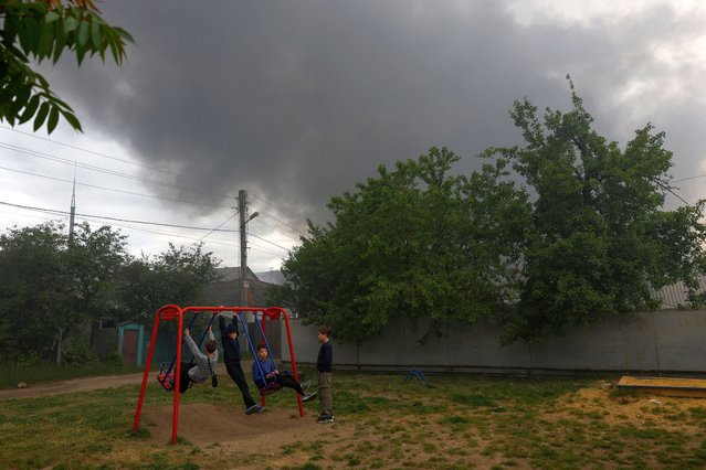 Boys play at a playground while smoke rises after a Russian missile strike, amid Russia's attack on Ukraine, in Kharkiv, Ukraine on May 17, 2024. (Photo by Valentyn Ogirenko/Reuters)