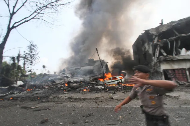 A police officer gestures at the crowd near the site where an Air Force cargo plane crashed in Medan, North Sumatra, Indonesia, Tuesday, June 30, 2015. An Indonesian Air Force Hercules C-130 plane with 12 crew aboard has crashed into a residential neighborhood in the country's third-largest city Medan. (Photo by Gilbert Manullang/AP Photo)