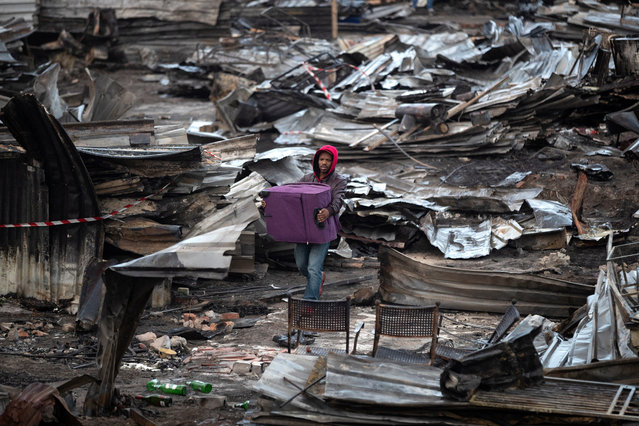 A resident of Masiphumelele informal settlement walks with his salvaged belongings through burned shacks after a fire destroyed over 250 structures in Masiphumelele, Cape Town, South Africa, 29 July 2019. One person died and over a thousand people were left homeless after a fire swept through Masiphumelele’s wetland informal settlement in E-Section in the early hours of 29 July 2019. According to residents the fire was caused by a candle in one of the shacks. The high density living conditions and strong winds caused the fire to spread rapidly. Disaster Risk Management is assisting survivors with food, shelter and help with arranging new documents destroyed in the fire. Many displaced residents have sought shelter in the community hall with freezing temperatures expected as another cold front sweeps over the cape. (Photo by Nic Bothma/EPA/EFE)