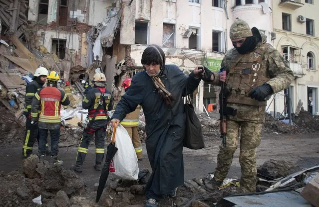 A volunteer of the Ukrainian Territorial Defense Forces assists a woman to cross the street in Kharkiv, Ukraine, Wednesday, March 16, 2022. (Photo by Andrew Marienko/AP Photo)