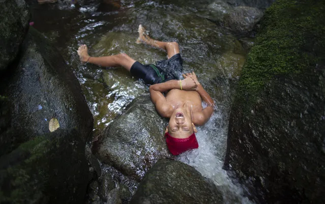 In this photo taken October 12, 2019, a youth lies in water for a cleansing ritual on Sorte Mountain where followers of indigenous goddess Maria Lionza gather annually in Venezuela's Yaracuy state. Believers congregated for rituals on the remote mountainside where adherents make the pilgrimage to pay homage to the goddess, seeking spiritual connection and physical healing. (Photo by Ariana Cubillos/AP Photo)