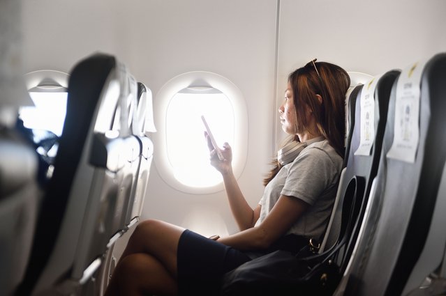 Business woman using her phone on a plane. (Photo by Carlina Teteris/Getty Images)