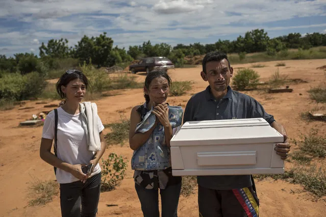 Roberto Parra carries the remains of his son Matias Alejandro alongside his wife Maria Isabel Parra and daughter Alejandra Parra at San Sebastian municipality cemetery before burying him in Maracaibo, Venezuela, November 27, 2019. Parra said his 19-day-old boy died after he was born with lung problems at a public hospital, where, after his wife was turned away from the first hospital, was left to deliver alone in a dirty chair before doctors rushed her up the stairs with her baby's head already exposed. Although the baby was born with respiratory problems, they were told to take him home because he could get sicker if they stayed. (Photo by Rodrigo Abd/AP Photo)