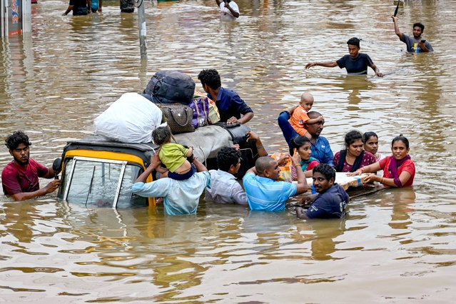 People carry their belongings as they wade through a flooded street after heavy monsoon rains, in Vijayawada on September 2, 2024. Intense monsoon rains and floods in India's southern states have killed at least 25 people, with thousands rescued and taken to relief camps, disaster officials said on September 2. (Photo by Chandu Lumburu/AFP Photo)