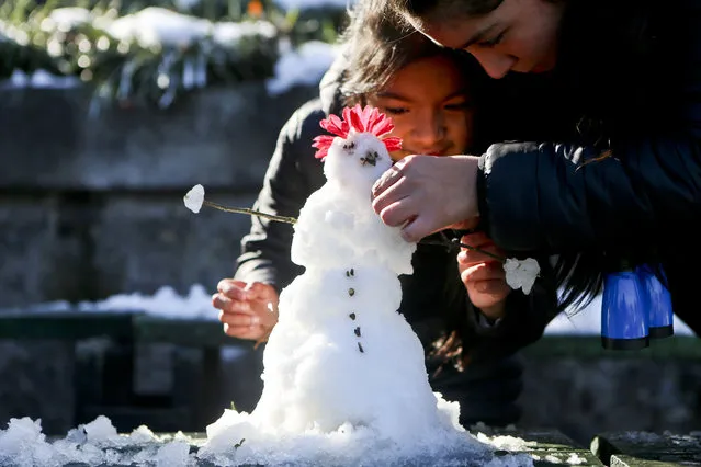 Girls make a snowman at San Cristobal hill in Santiago, Chile, Sunday, July 16, 2017. Chile's capital was blanketed this weekend by the biggest snowfall in decades, with some residents grumbling about blocked roads and downed power lines, while others made snowmen or tossed snowballs. (Photo by Esteban Felix/AP Photo)