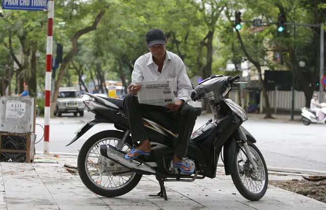 In this Wednesday, June 21, 2017, photo, Nguyen Kim Lan reads a newspaper as he waits for customers at an intersection in Hanoi, Vietnam. Lan, 62-year-old traditional motorbike taxi driver, or Xe Om, used to make a decent living shuttling customers, but his clientele has dwindled as young and tech-savvy Vietnamese increasingly use ride-hailing apps like Uber and Grab to summon cheaper, safer motorbike taxis. (Photo by Tran Van Minh/AP Photo)