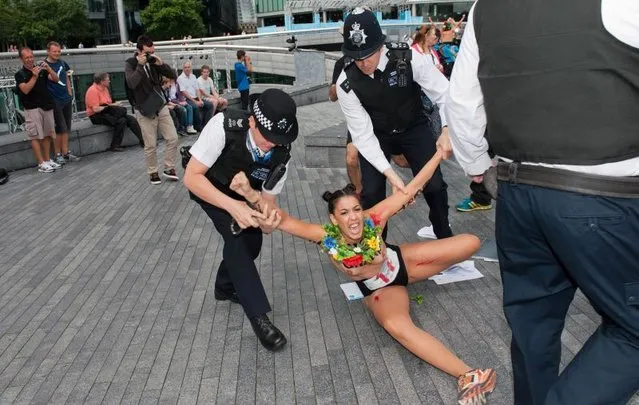 British policemen block a topless activist of Ukraine's prominent feminist rights group FEMEN as she was protesting near the Tower Bridge in Central London on August 2, 2012 on day 6 of the London 2012 Olympic games. FEMEN's activists organised an “islamic maraton” to demonstrate against “islamic regimes” they say being supported by the International Olympic Committee. (Photo by Will Oliver/AP Photo)