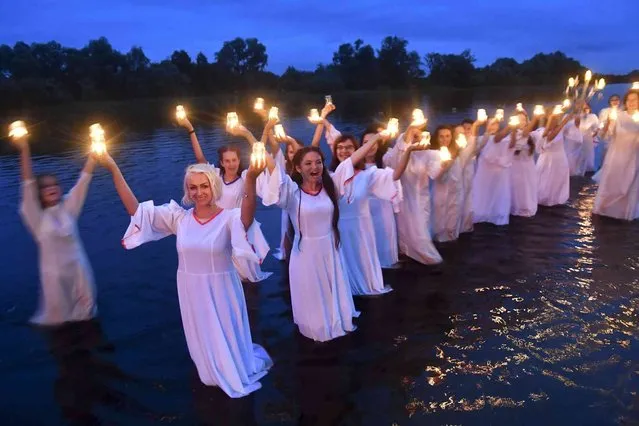 Belarusian girls holding candles stand at the Berezina river on Ivan Kupala Day, an ancient night long celebration marking the Summer Solstice, the shortest night of the year, in Parichi village, some 200 km (125 miles) south of Parichi , Belarus, Wednesday, July 6, 2022. Ivan Kupala or St. John's Day or Midsummer Day, is a traditional carnival, which centers around a bonfire with plenty of food and dancing. (Photo by Viktor Drachev/AP Photo)