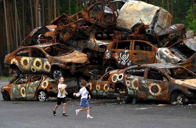 Children play at the symbolic cemetery of cars shot by Russian troops,some painted by local artists, in Irpin, on August 9, 2022, amid Russian invasion of Ukraine. (Photo by Sergei Supinsky/AFP Photo)