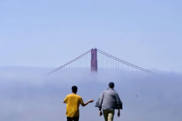 Pedestrians walk on a hill in front of the Golden Gate Bridge partially covered by fog in San Francisco, Tuesday, August 16, 2022. (Photo by Jeff Chiu/AP Photo)