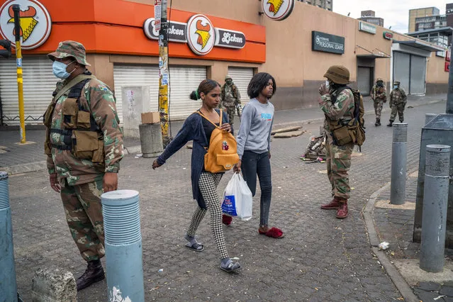 Residents returning from food shopping walk past South African National Defense Forces patrolling in downtown Johannesburg on Monday March 30, 2020. South Africa went into a nationwide lockdown for 21 days in an effort to control the spread of the coronavirus, and patrols have increased in the streets to enforce the lockdown. (Photo by Jerome Delay/AP Photo)