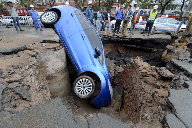 Workers look on as a car is stranded in a sinkhole on a street in Lanzhou, Gansu province, China, September 9, 2015. The driver managed to get out of the car unharmed and no one was injured during the incident, local media reported. (Photo by Reuters/Stringer)