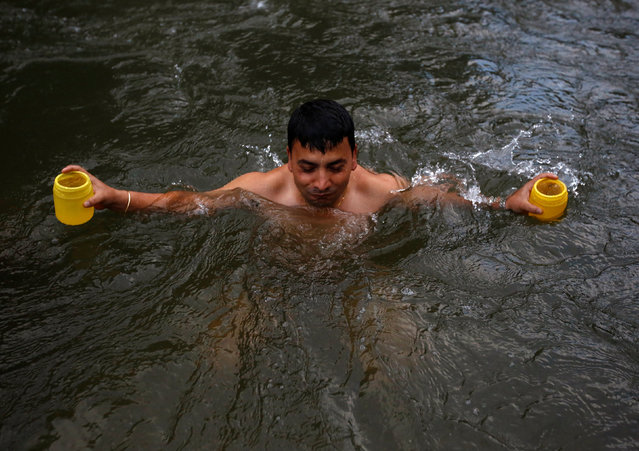 A devotee emerges holding plastic bottles filled with water, which is considered holy, from the Bagmati River during the “Bol Bom” (Say Shiva) pilgrimage in Kathmandu, Nepal, August 8, 2016. (Photo by Navesh Chitrakar/Reuters)