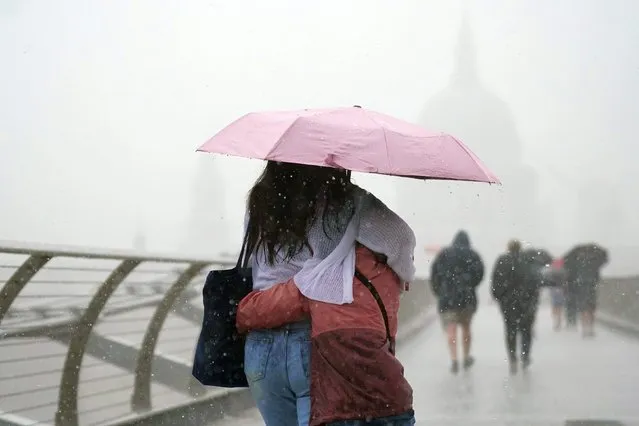People with umbrellas walking in the rain on Millennium Bridge, London, Wednesday August 17, 2022.. After weeks of sweltering weather, which has caused drought and left land parched, the Met Office's yellow thunderstorm warning forecasts torrential rain and thunderstorms that could hit parts England and Wales. (Photo by Victoria Jones/PA Wire via AP Photo)