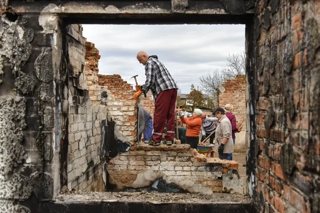Volunteers  clean the debris of a house, destroyed in combat action in Novoselivka village, Chernihiv region, Ukraine, 29 October 2022. A group of local people from Chernihiv and the nearby village Novoselivka, whose houses were destroyed or damaged during the Russian invasion, gathered to help each other to clean the debris of their houses and to restore them. As soon as people came back to their settlements the movement grew and transformed into the volunteer organization “Bo Mozhemo” (Because we can) to which, more and more people, not only from Chernihiv but also from nearby towns and villages, join. The works focus also on reparing the roofs before upcoming winter. (Photo by Oleg Petrasyuk/EPA/EFE)