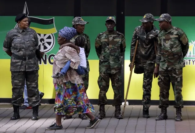 A woman carrying a child on her back, walks past the members of the former military wing of the ANC called MK, outside the ruling party ANC headquarters in downtown Johannesburg, South Africa, Monday, September 5, 2016. A group of ANC members planning to occupy the organisation's headquarters' Luthuli House' on Monday' have reiterated their call that President Jacob Zuma resign and that the national executive committee resign. (Photo by Themba Hadebe/AP Photo)