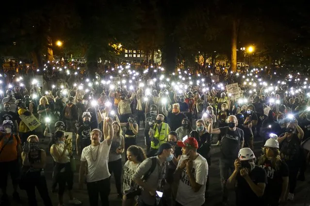 Demonstrators raise their cell phone lights as they chant slogans during a Black Lives Matter protest at the Mark O. Hatfield United States Courthouse Wednesday, July 29, 2020, in Portland, Ore. (Photo by Marcio Jose Sanchez/AP Photo)