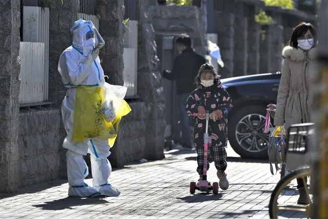 A child wearing a face mask and riding on a scooter passes by a worker in protective suit on his way to collect COVID samples from the lockdown residents in Beijing, Thursday, December 1, 2022. More cities eased anti-virus restrictions as Chinese police tried to head off protests Thursday while the ruling Communist Party prepared for the high-profile funeral of the late leader Jiang Zemin. (Photo by Andy Wong/AP Photo)
