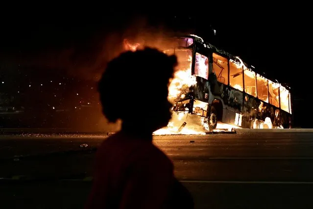A woman walks near a bus on fire as supporters of Brazil's President Jair Bolsonaro protest after supreme court justice Alexandre de Moraes ordered a temporary arrest warrant of indigenous leader Jose Acacio Serere Xavante for alleged anti-democratic acts, in Brasilia, Brazil on December 12, 2022. (Photo by Ueslei Marcelino/Reuters)