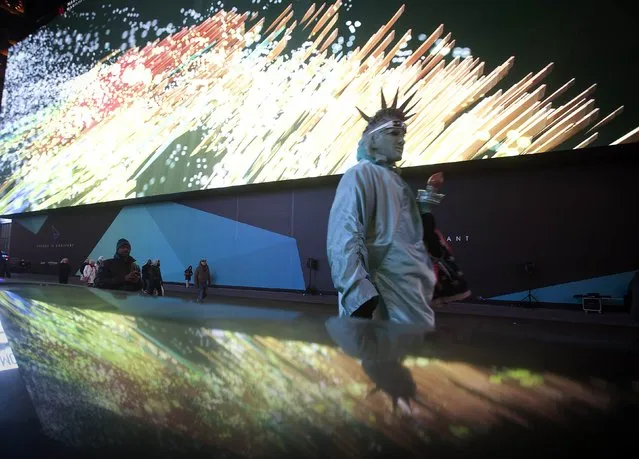 A man dressed up as the Statue of Liberty walks in front of a new digital advertising screen in Times Square, New York, November 18, 2014. According to local media the screen is a full block long, 8 stories tall, is lit with 24 million LED pixels and has a higher resolution than most TV sets. The advertising rate is reported at $2.5 million USD for a four-week run making it one of the most expensive outdoor advertising spaces in the world. (Photo by Carlo Allegri/Reuters)