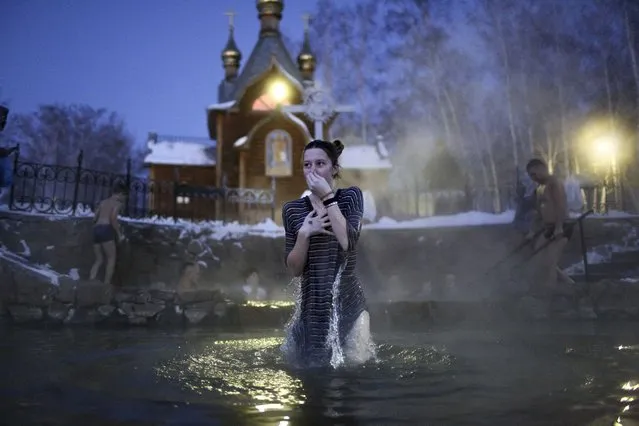 A woman bathes in water during a traditional Epiphany celebration as the temperature dropped to about –12 degrees (10,4 degrees Fahrenheit) near the Achairsky monastery outside the Siberian city of Omsk, Russia, early Thursday, January 19, 2023. Across Russia, the devout and the daring are observing the Orthodox Christian feast day of Epiphany by immersing themselves in frigid water through holes cut through the ice of lakes and rivers. Epiphany celebrates the revelation of Jesus Christ as the incarnation of God through his baptism in the River Jordan. (Photo by Evgeniy Sofiychuk/AP Photo)